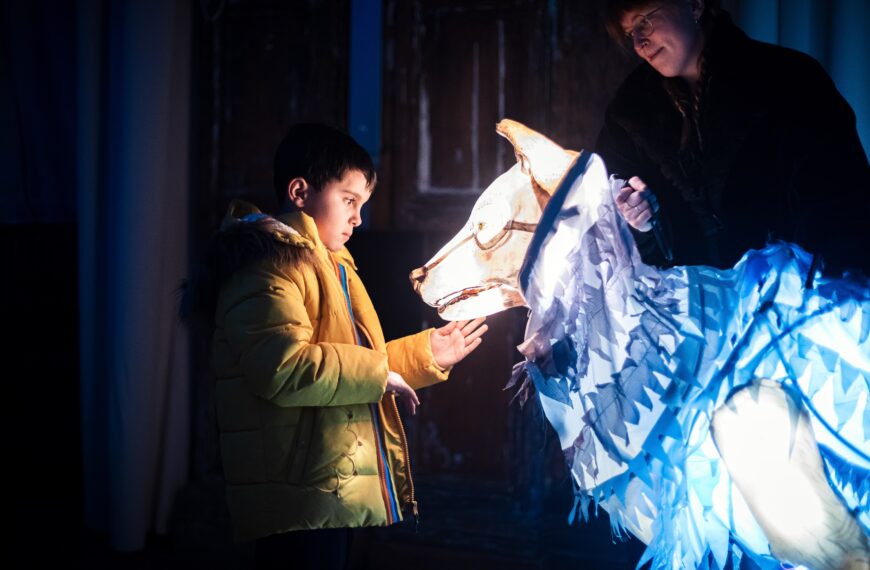 A child looks at an illuminated puppet of a wolf.